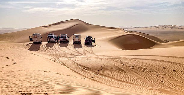 A group of 4x4 campers are lined up on the crest of a sand dune somewhere in the Admer erg, in the heart of the Algerian Sahara desert.