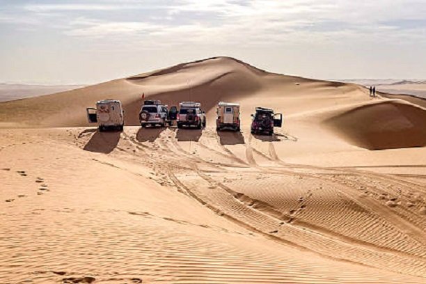 A group of 4x4 campers are lined up on the crest of a sand dune somewhere in the Admer erg, in the heart of the Algerian Sahara desert.