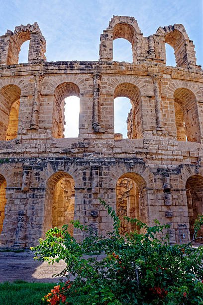 Medium shot showcasing the towering, crumbling stone walls and open archways of the Roman Amphitheatre of El Jem in Tunisia under a bright blue sky on 07.10.2024